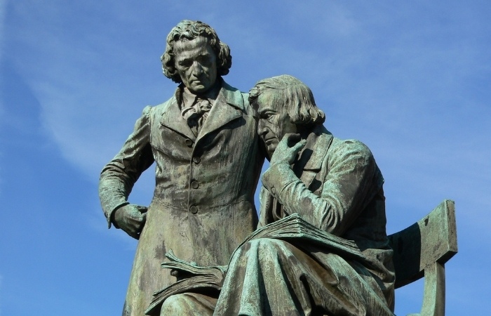 looking up at a statue of the Borthers Grimm in Germany with blue sky in the background